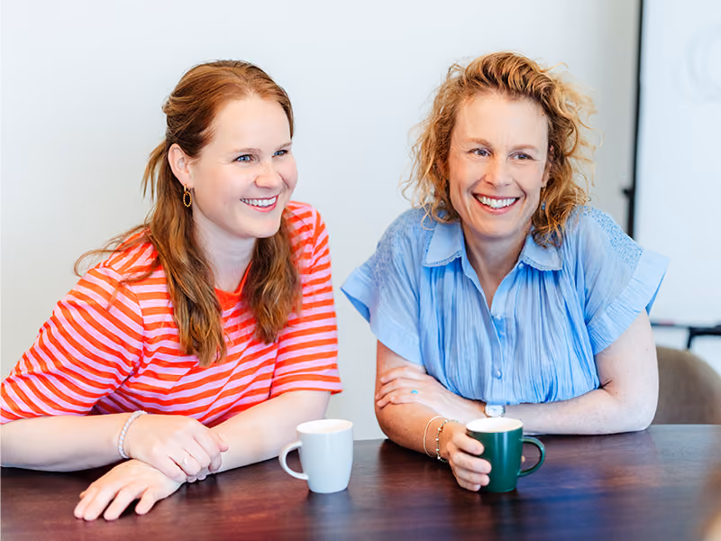 Twee vrouwen lachen samen aan tafel met koffie, als beeld bij de relatietest van Voordeliefde