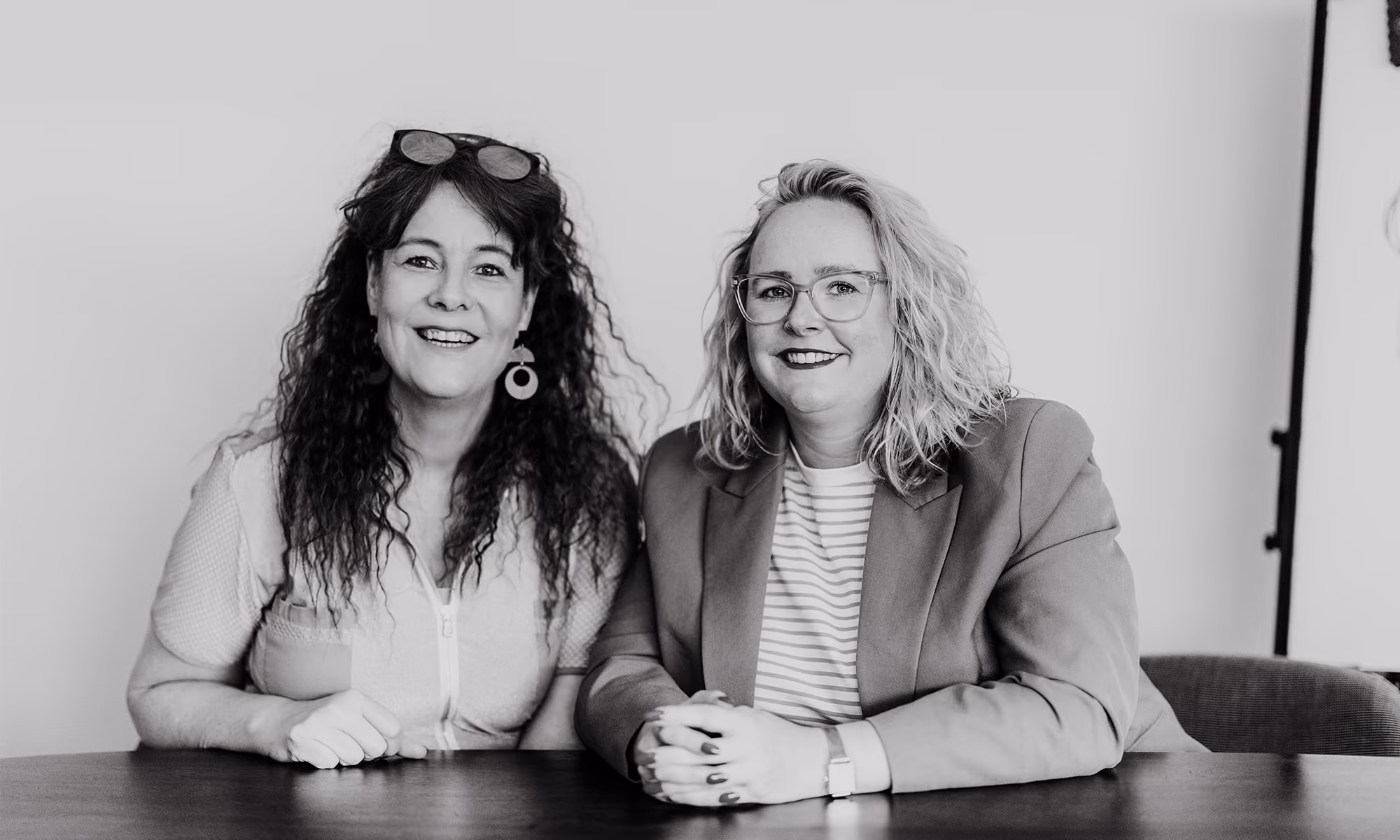 Zwart-witfoto van Carolien en Jolien, de relatiecounselors achter Voordeliefde, aan tafel