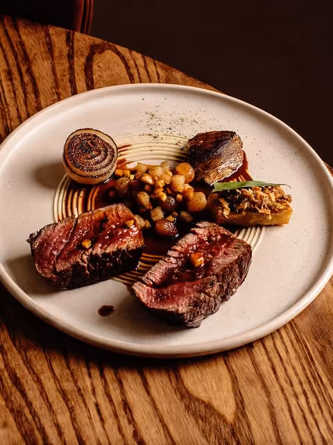 Plate with sliced grilled steak, chickpeas, roasted onion, and a stuffed vegetable garnish on a wooden table.