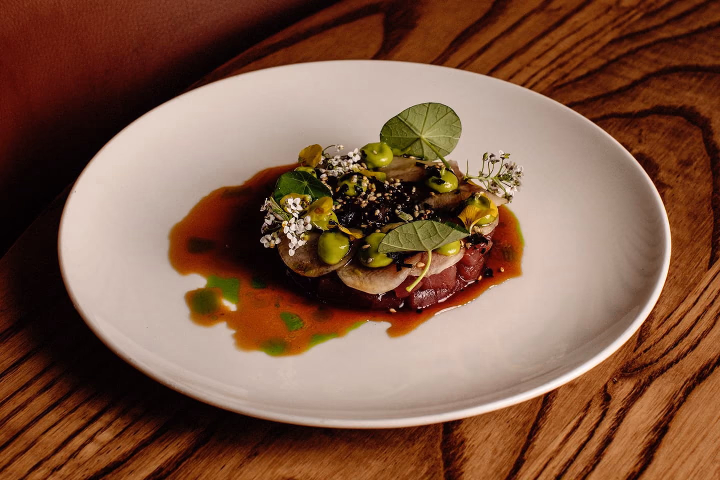 Gourmet dish with circular layers, green sauce dollops, and edible flowers on white plate.