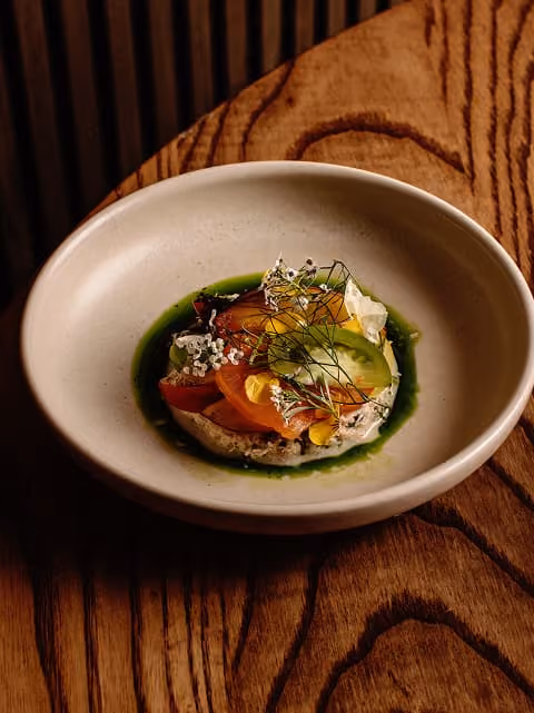 Gourmet dish with colorful vegetables and herbs in a beige bowl on a wooden table.