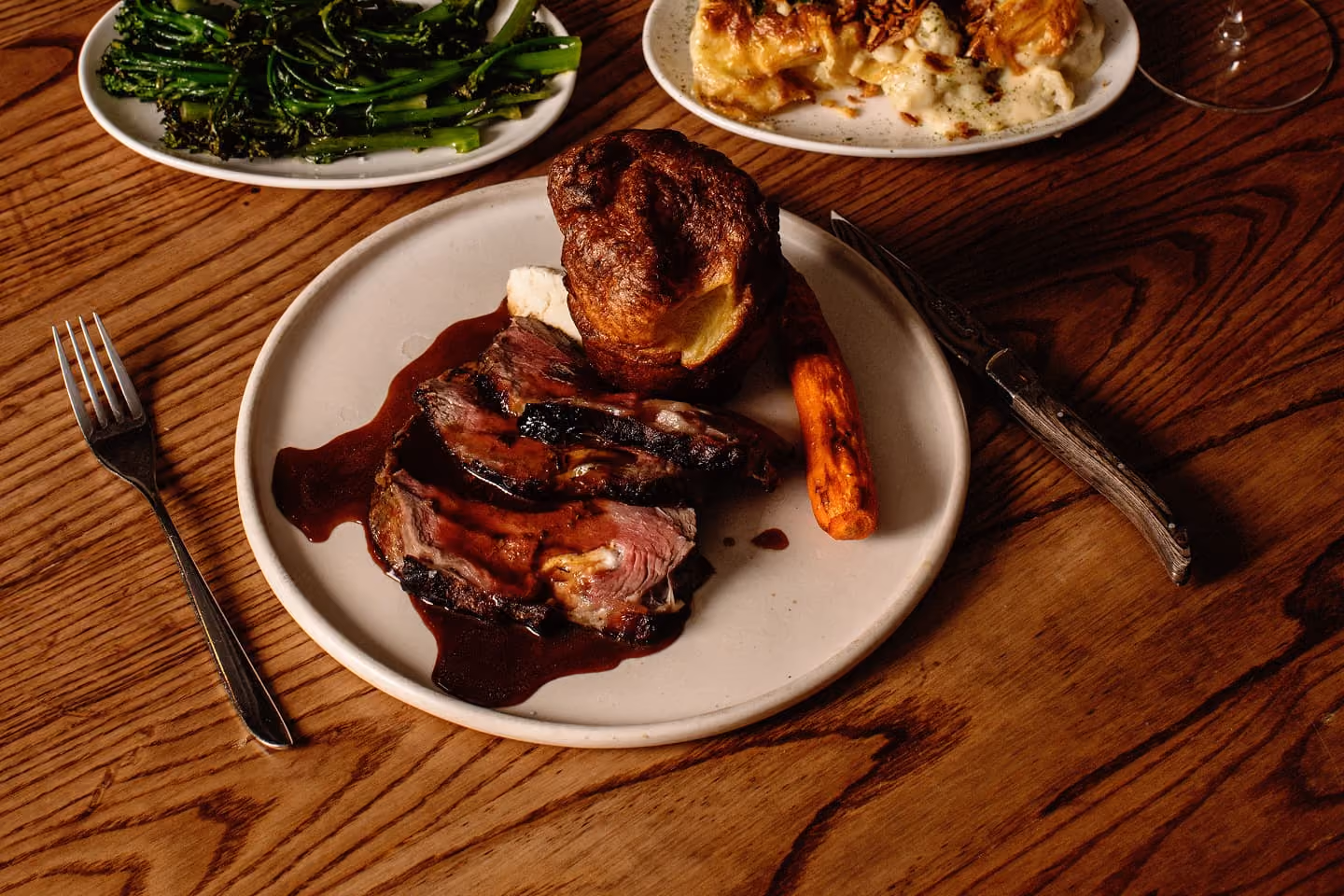 Plate with sliced roast beef, Yorkshire pudding, carrot, with side dishes of greens and potato bake.