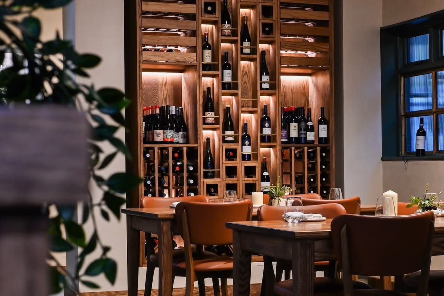 Cozy dining room with wooden tables, brown chairs, and a wall-mounted wine rack filled with bottles.