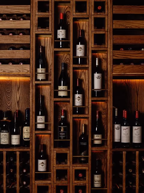 Wooden wine rack holding multiple bottles with dark labels under warm lighting.