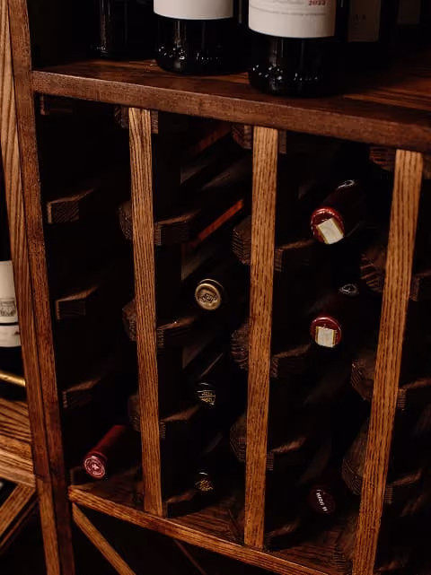 Wooden wine rack holding multiple bottles of red wine angled horizontally.