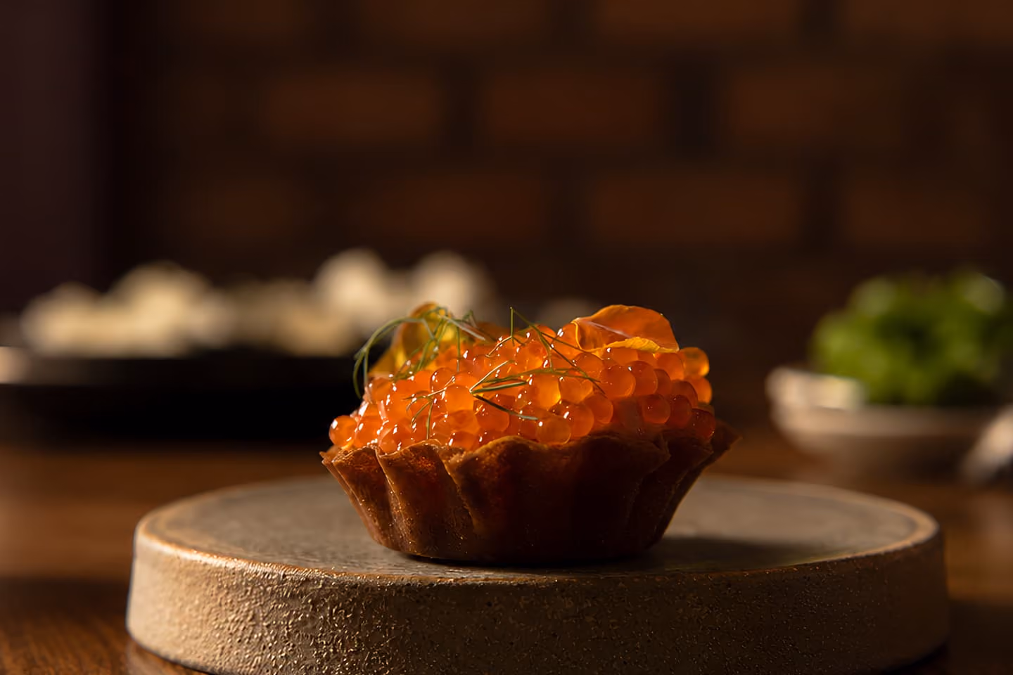 Close-up of a tart filled with orange fish roe garnished with herbs on a stone plate.