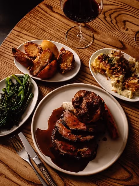 Chef pouring rich gravy over a slice of roast beef.