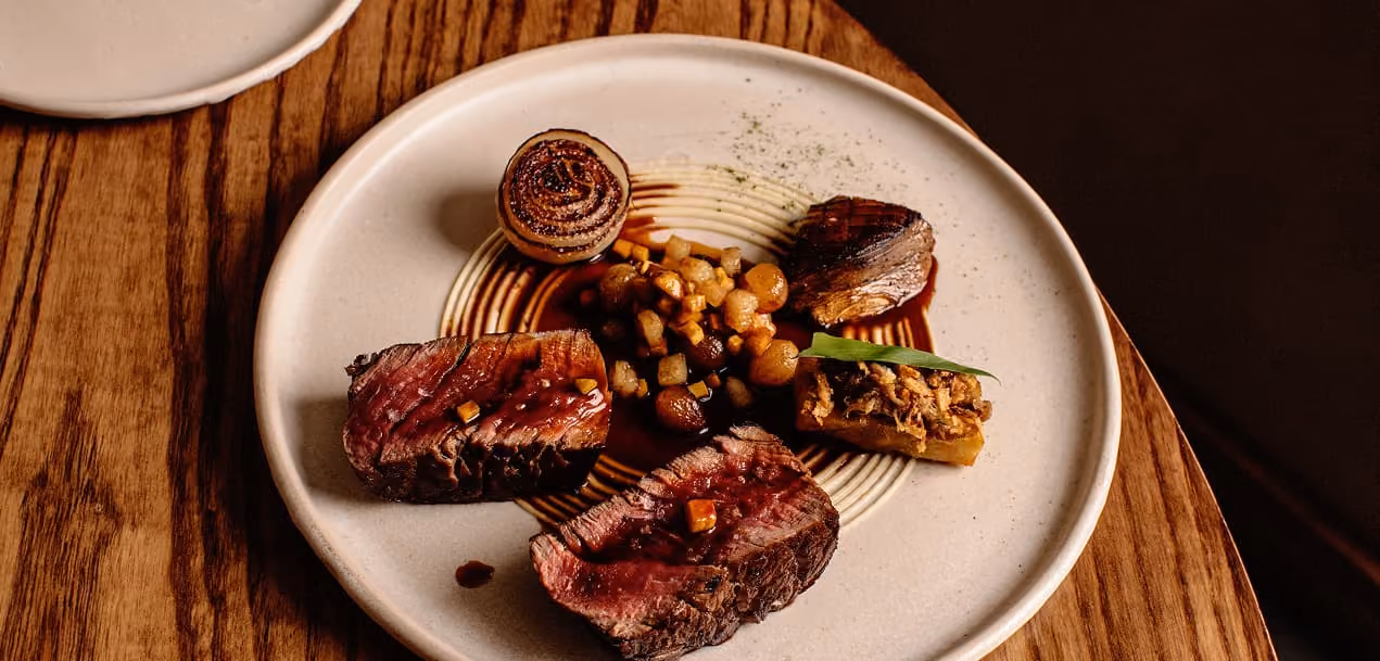 An array of à la carte dishes on ceramic plates served on a rustic wooden dining table.