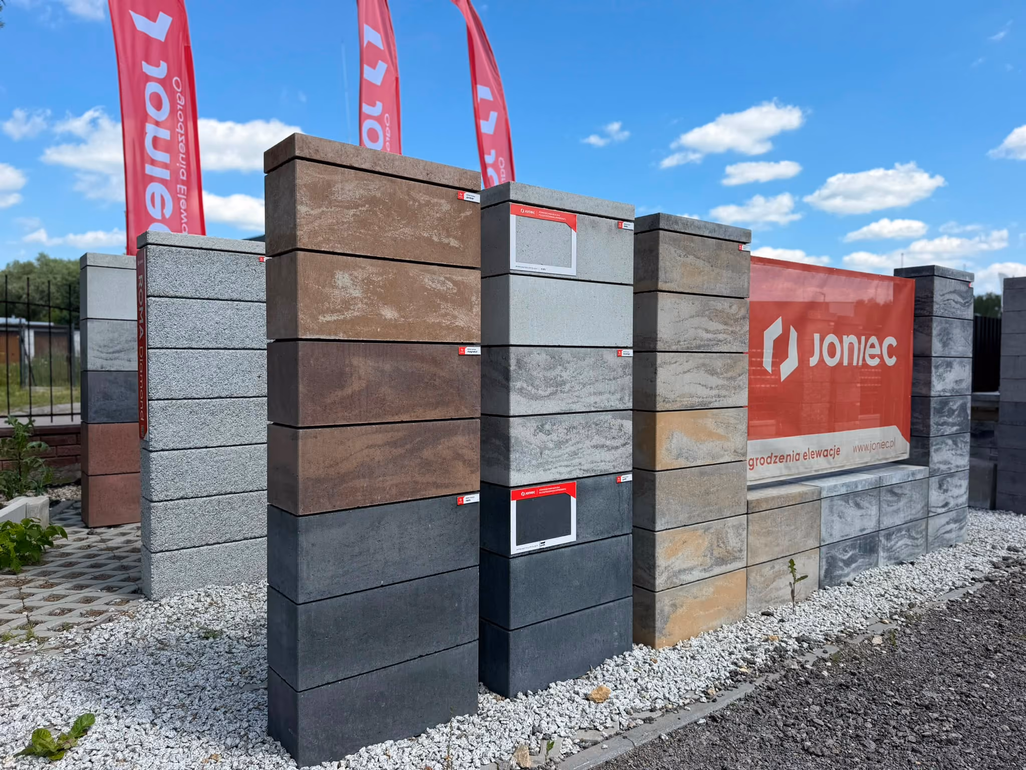 Outdoor display of various colored concrete blocks stacked in columns with Joniec banner behind them.