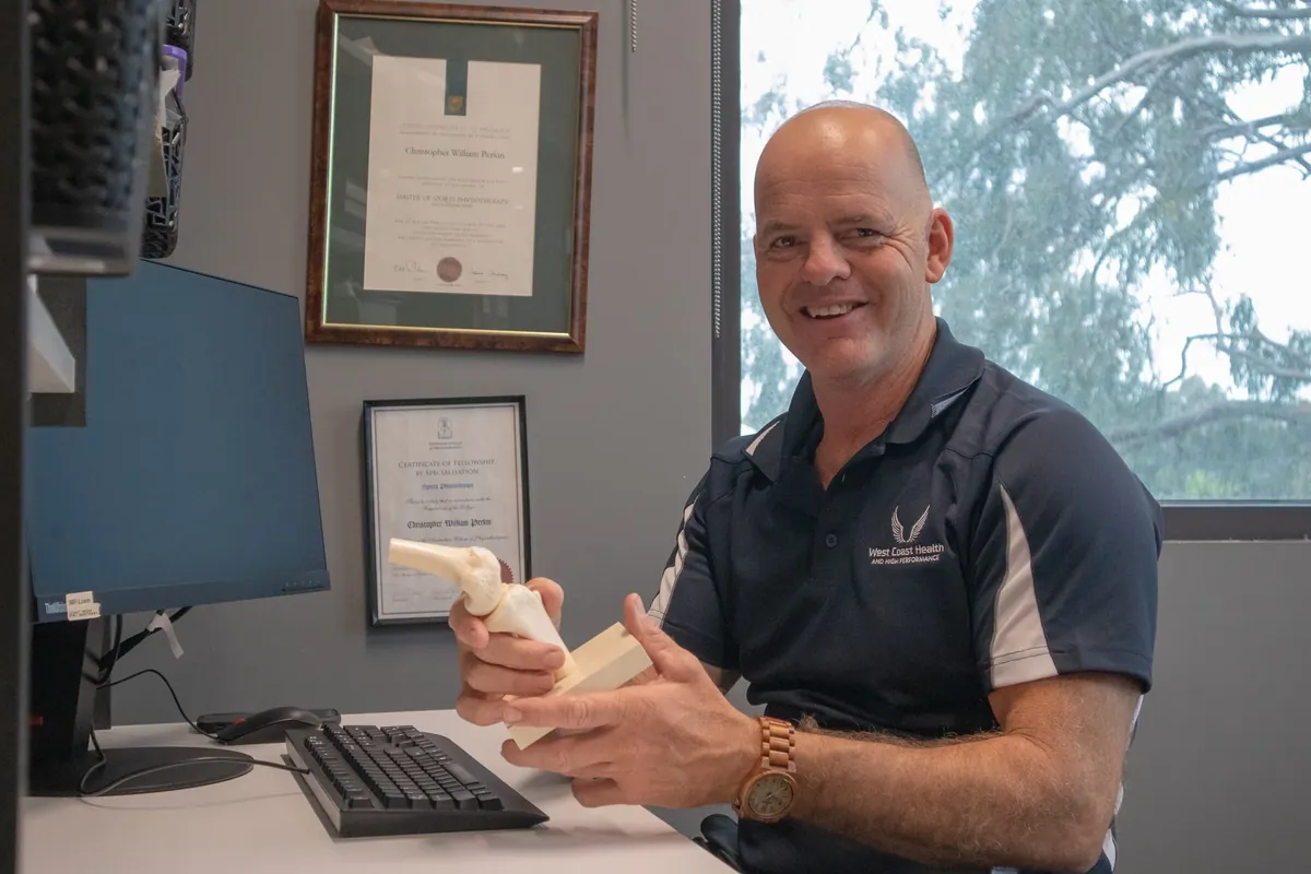 West Coast Health physiotherapist at the clinic desk holding an anatomical knee model