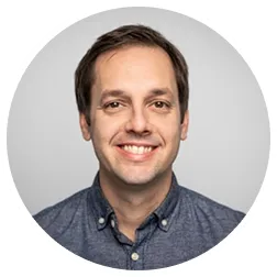 Portrait d'un homme souriant portant une chemise bleue, fond gris clair.