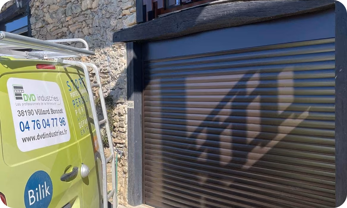 Véhicule vert avec logo DVD Industries stationné devant un bâtiment en pierre avec une porte de garage métallique.