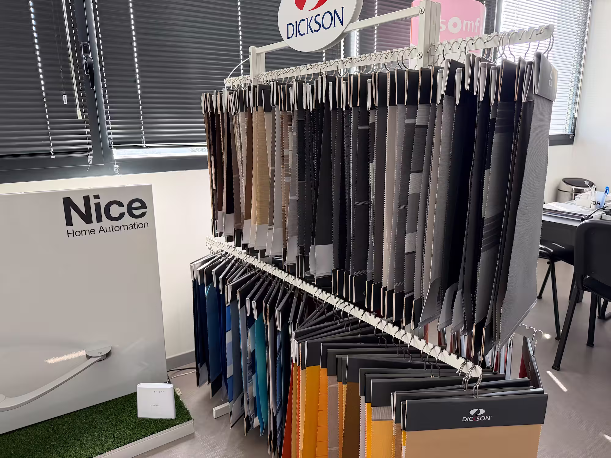 Échantillons de tissus suspendus dans un showroom avec des stores et un panneau Nice Home Automation.