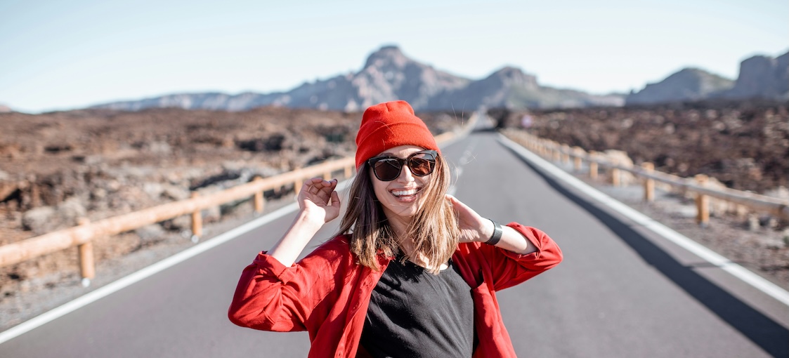 Woman turning back to look at the camera as she walks down an open road in the mountains