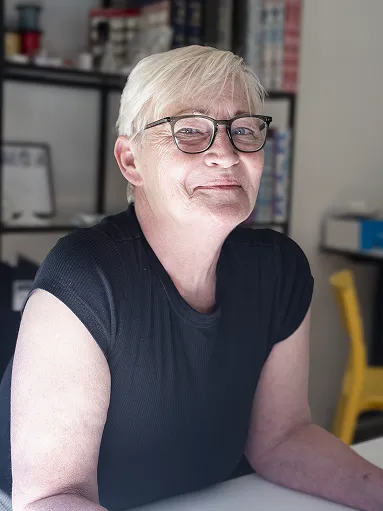 Smiling older woman with short white hair and glasses wearing a black shirt indoors.