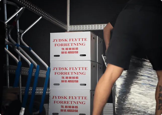 Stacked moving boxes labeled 'JYDSK FLYTTE FORRETNING' inside a van with a person handling items.