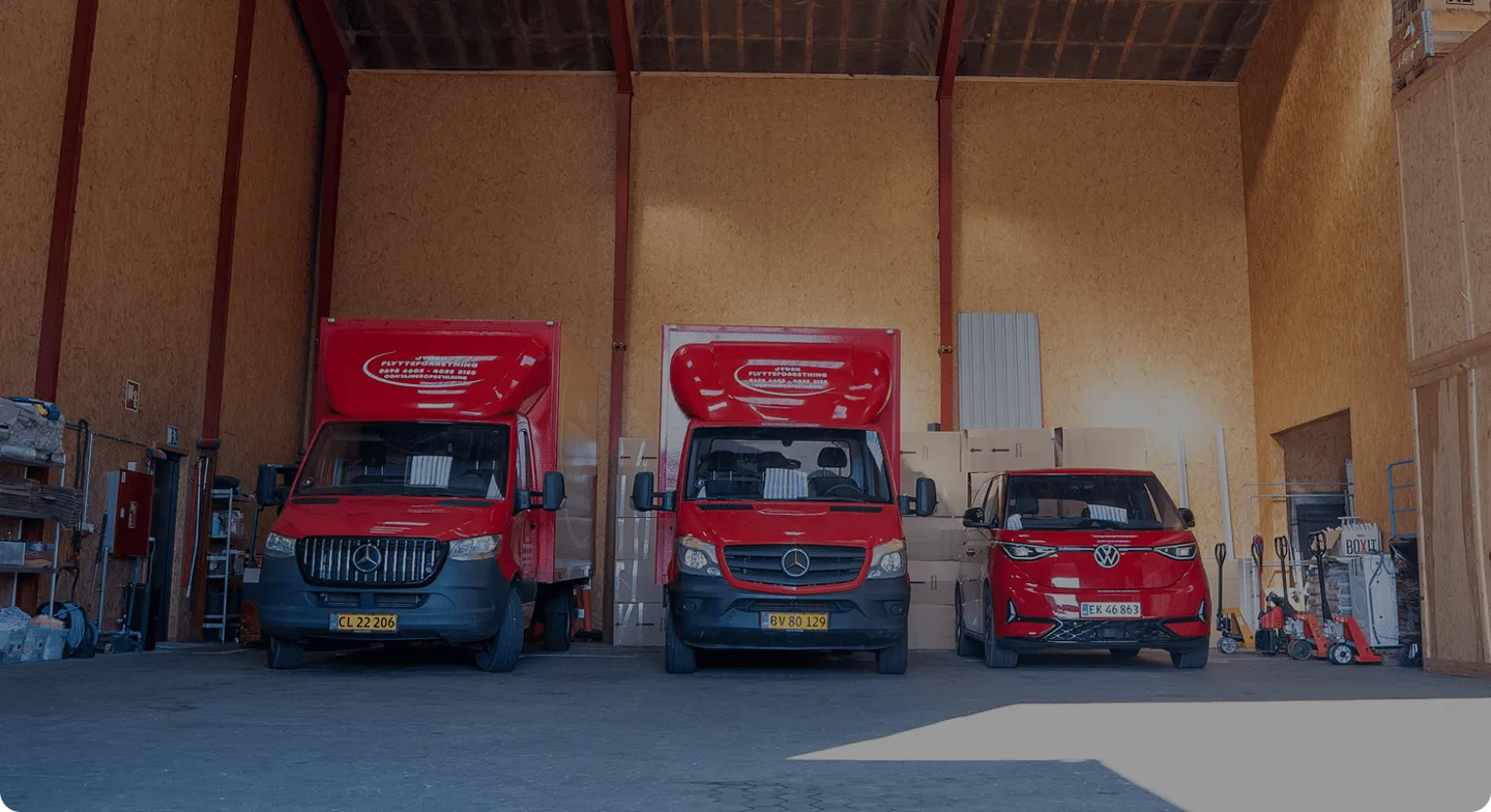 Three red vans parked inside a spacious warehouse with boxes and equipment around.