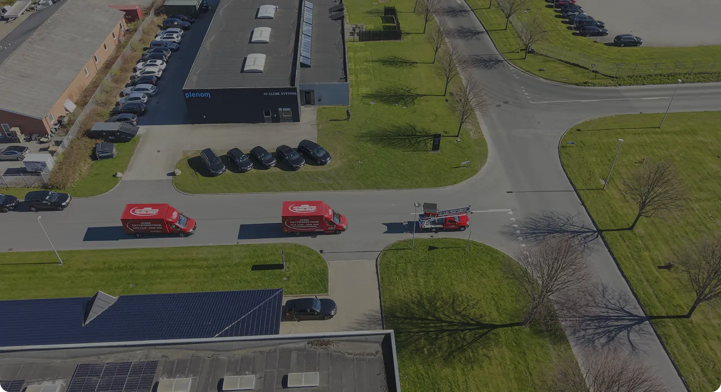 Aerial view of industrial area with parked cars and three red service vehicles driving on road.