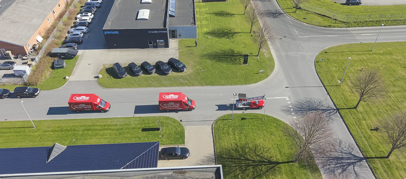 Aerial view of red vans and cars parked near commercial buildings with green lawns and shadows.