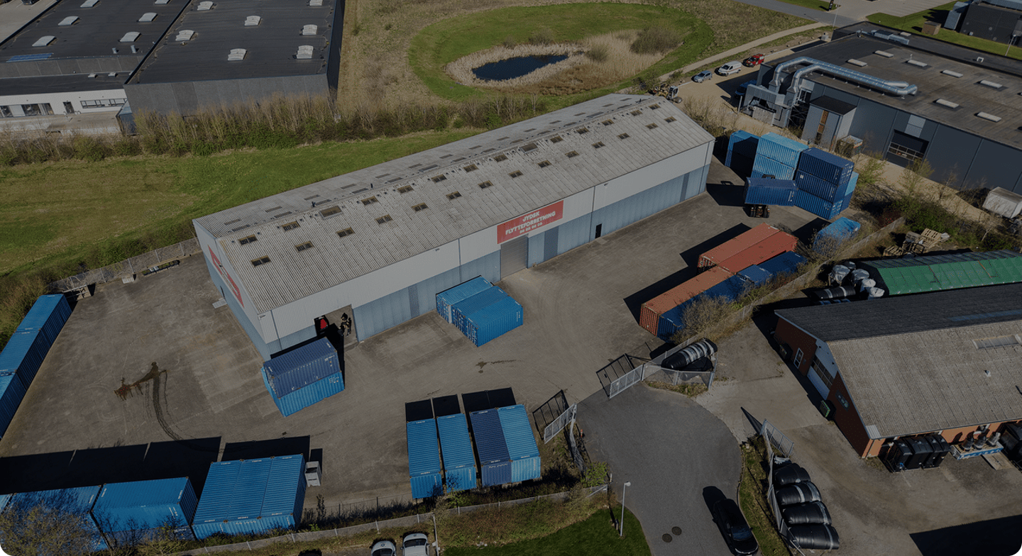 Aerial view of a warehouse surrounded by blue and red shipping containers and nearby buildings.