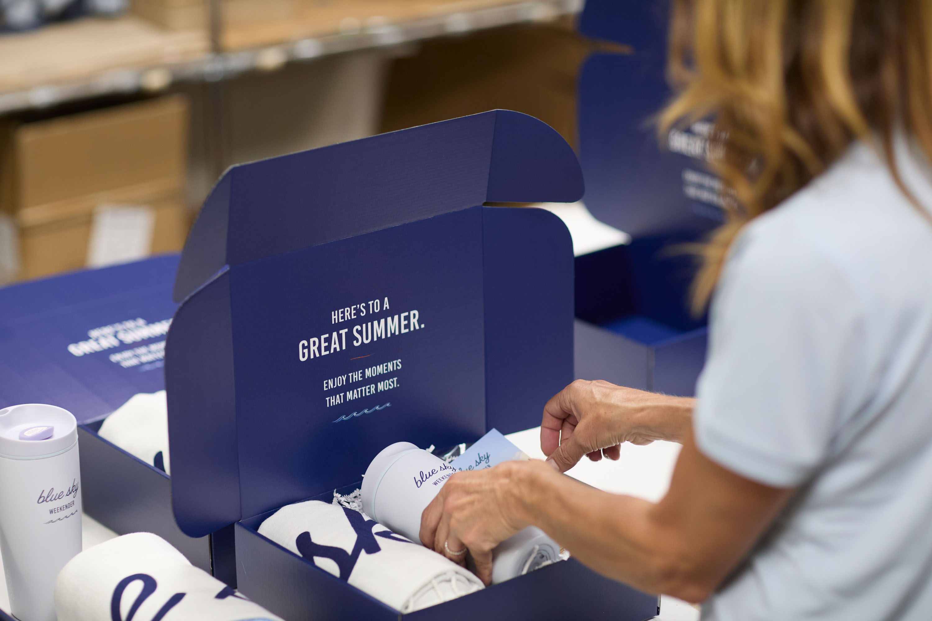 Blue Sky team member packing Blue Sky Weekender boxes with tumblers and towels