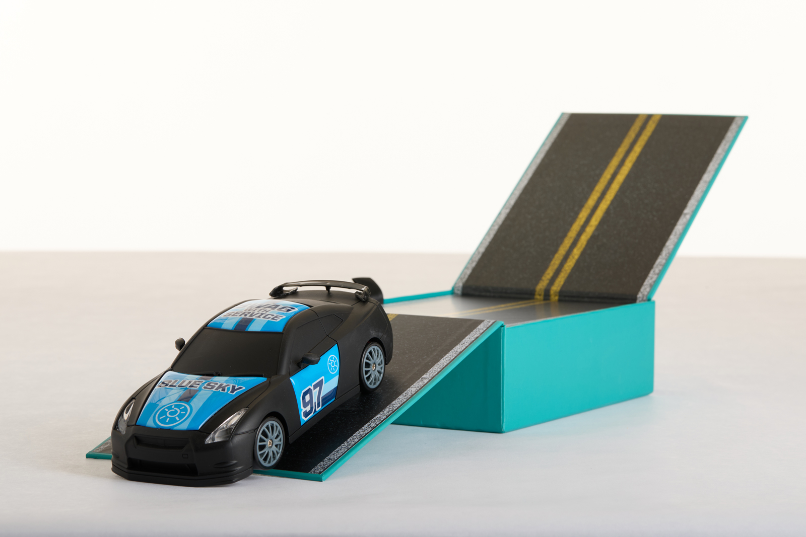 Teal Blue Sky gift box that unfolds into a printed road ramp, with a branded toy race car driving off it