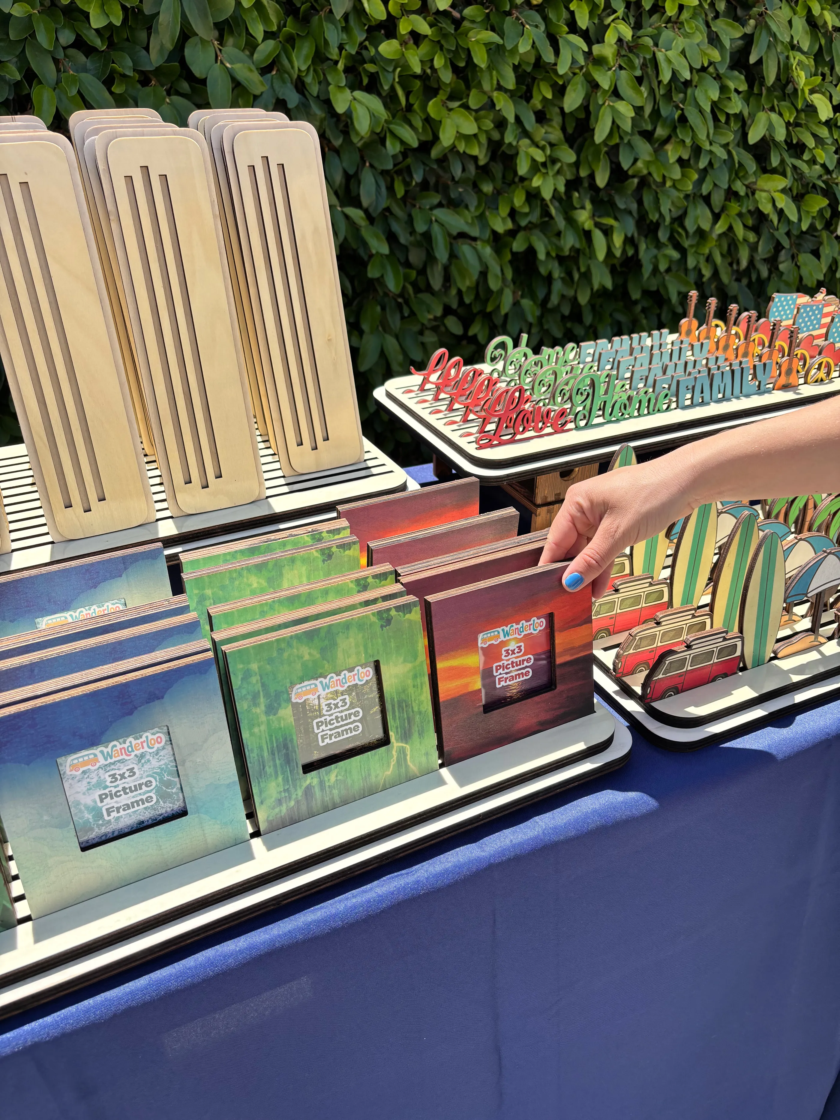 Hand reaching for a Wanderloo picture frame from a display of colorful frames and wooden bases