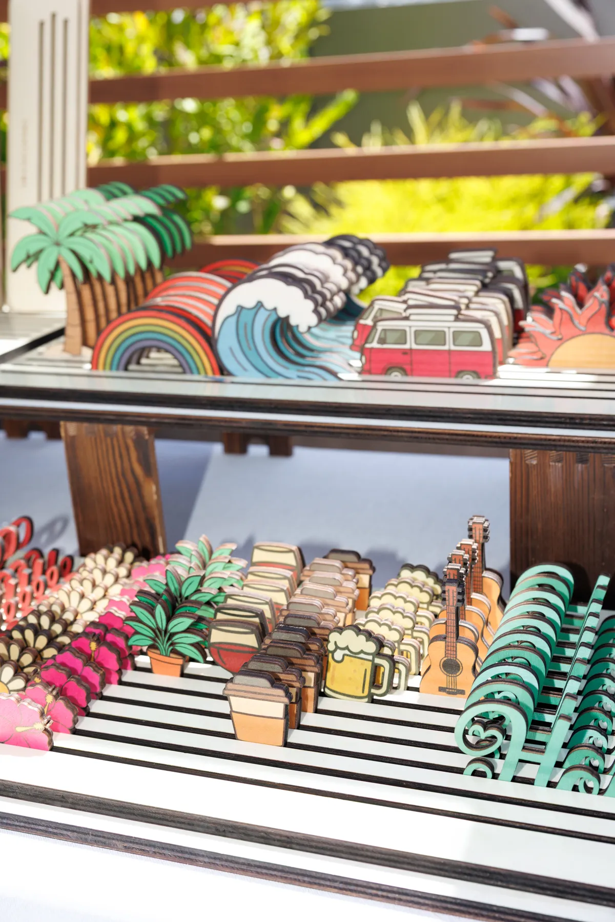 Trays of colorful Wanderloo charms including palm trees, rainbows, waves, vans, and guitars