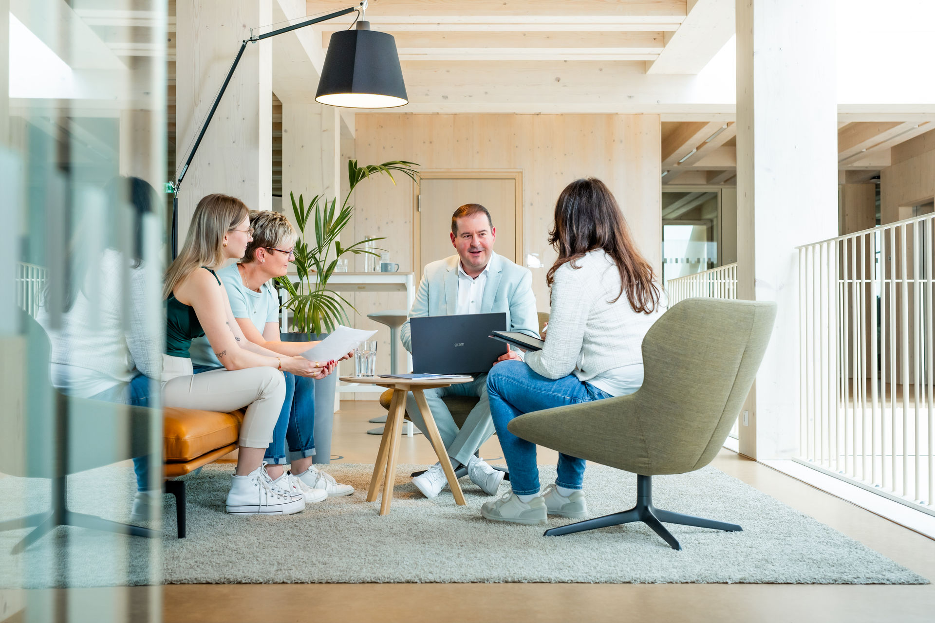 b+ GmbH Team beim informellen Meeting in hellem Büro mit Holzelementen.