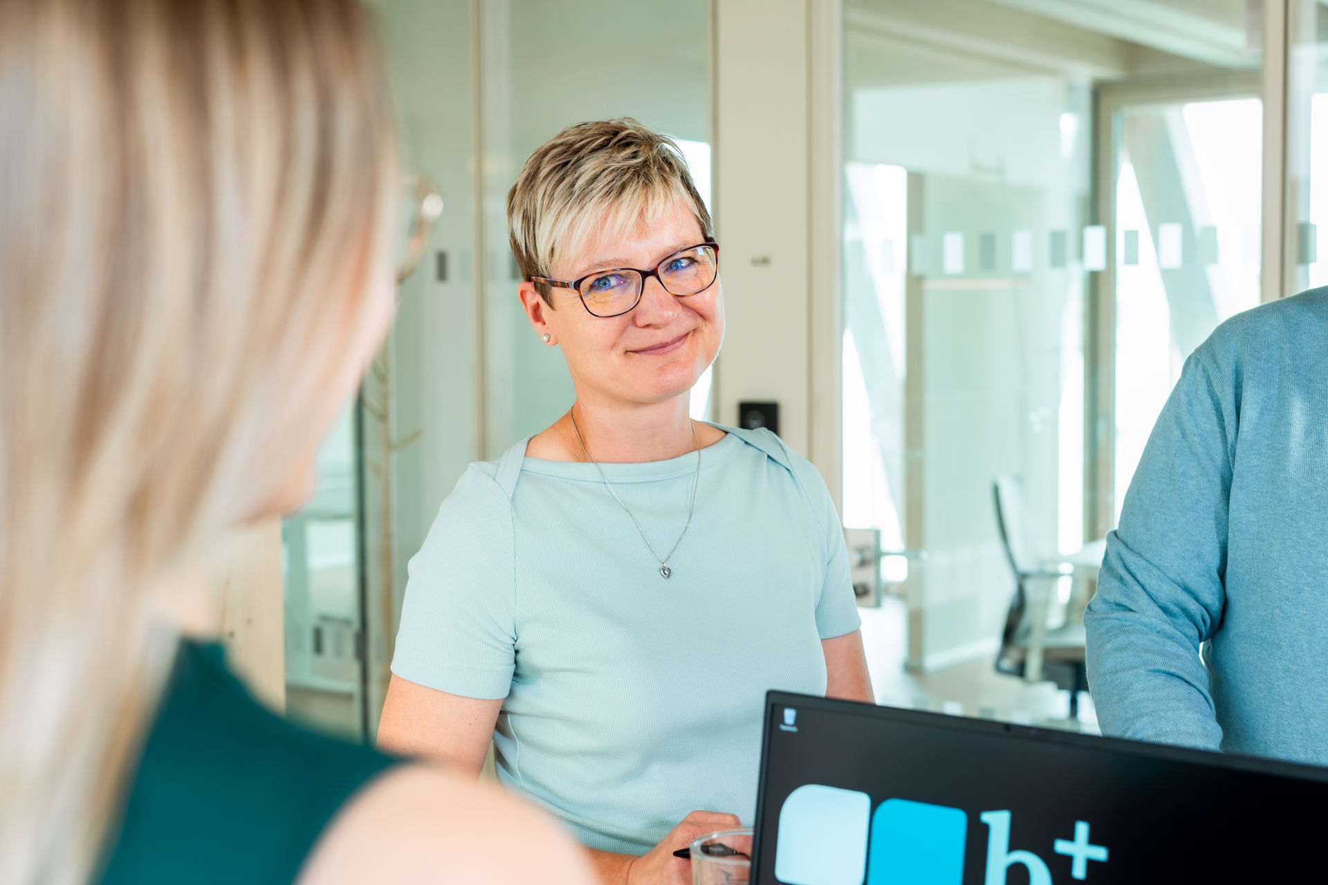 Frau mit kurzen Haaren und Brille in einem Besprechungsgespräch.