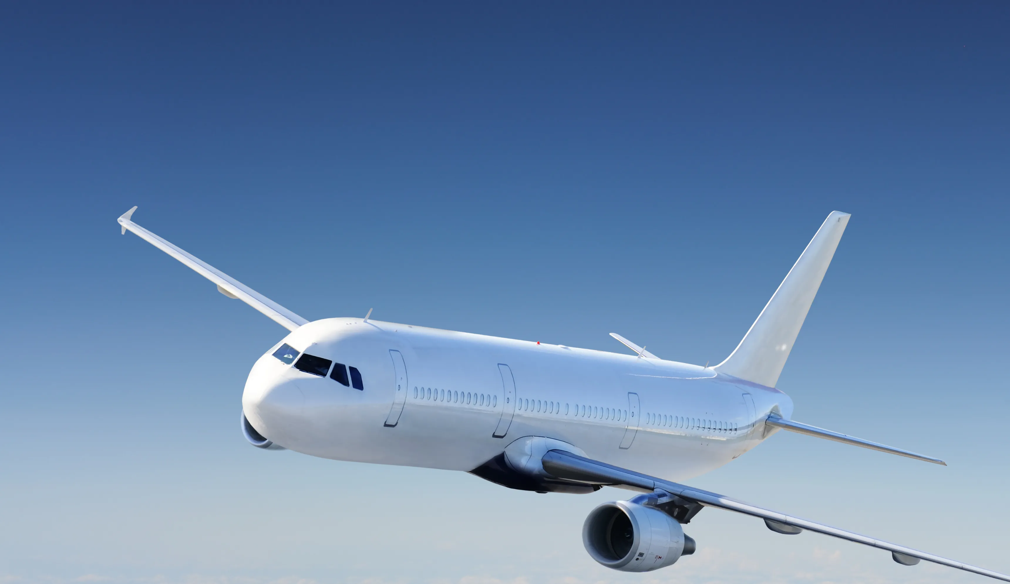 White commercial airplane flying in a clear blue sky at an angle showing the front and wing.