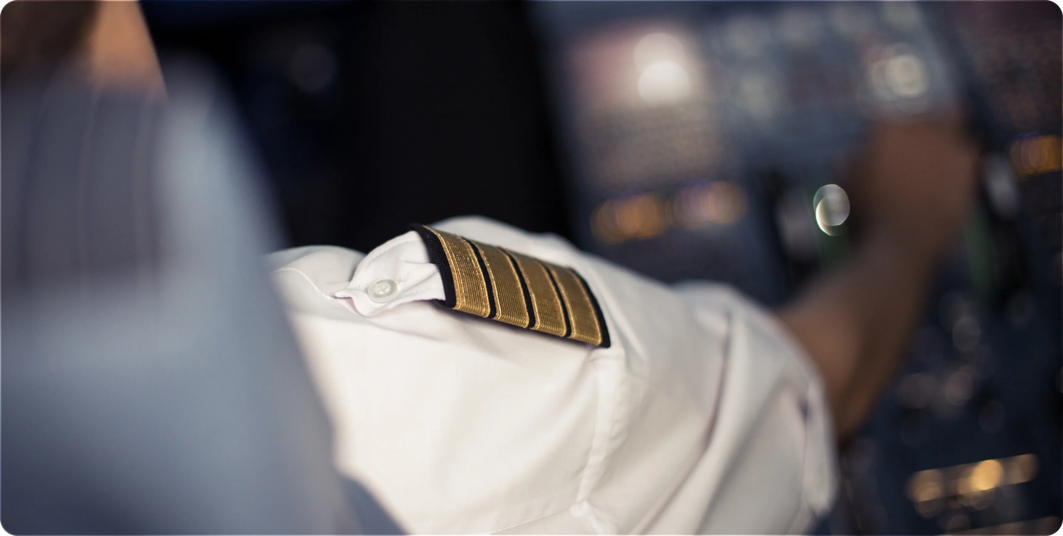 Close-up of a pilot's uniform shoulder with four gold stripes in a cockpit.