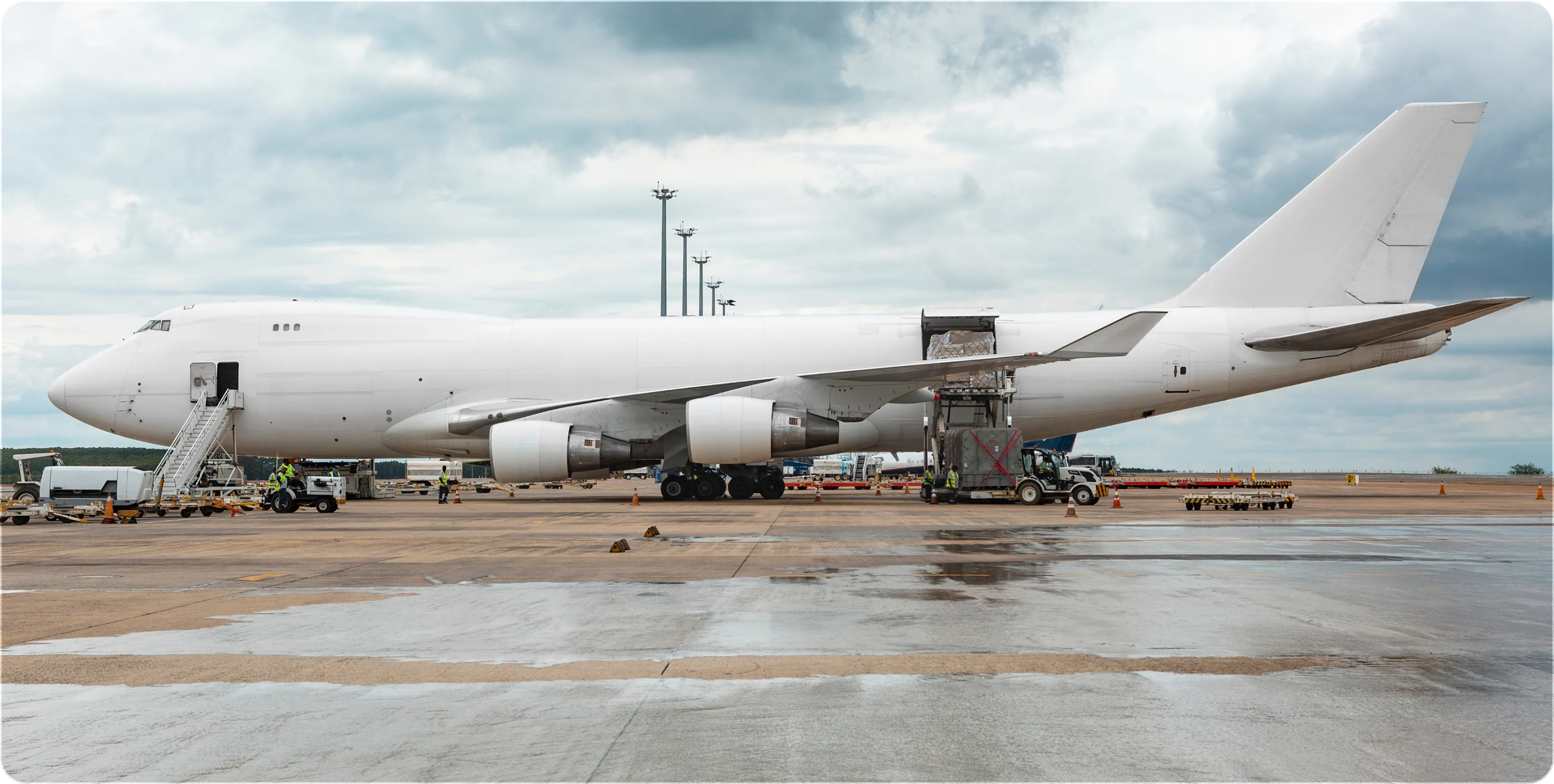 White cargo airplane on tarmac with open rear door unloading pallets under a cloudy sky.