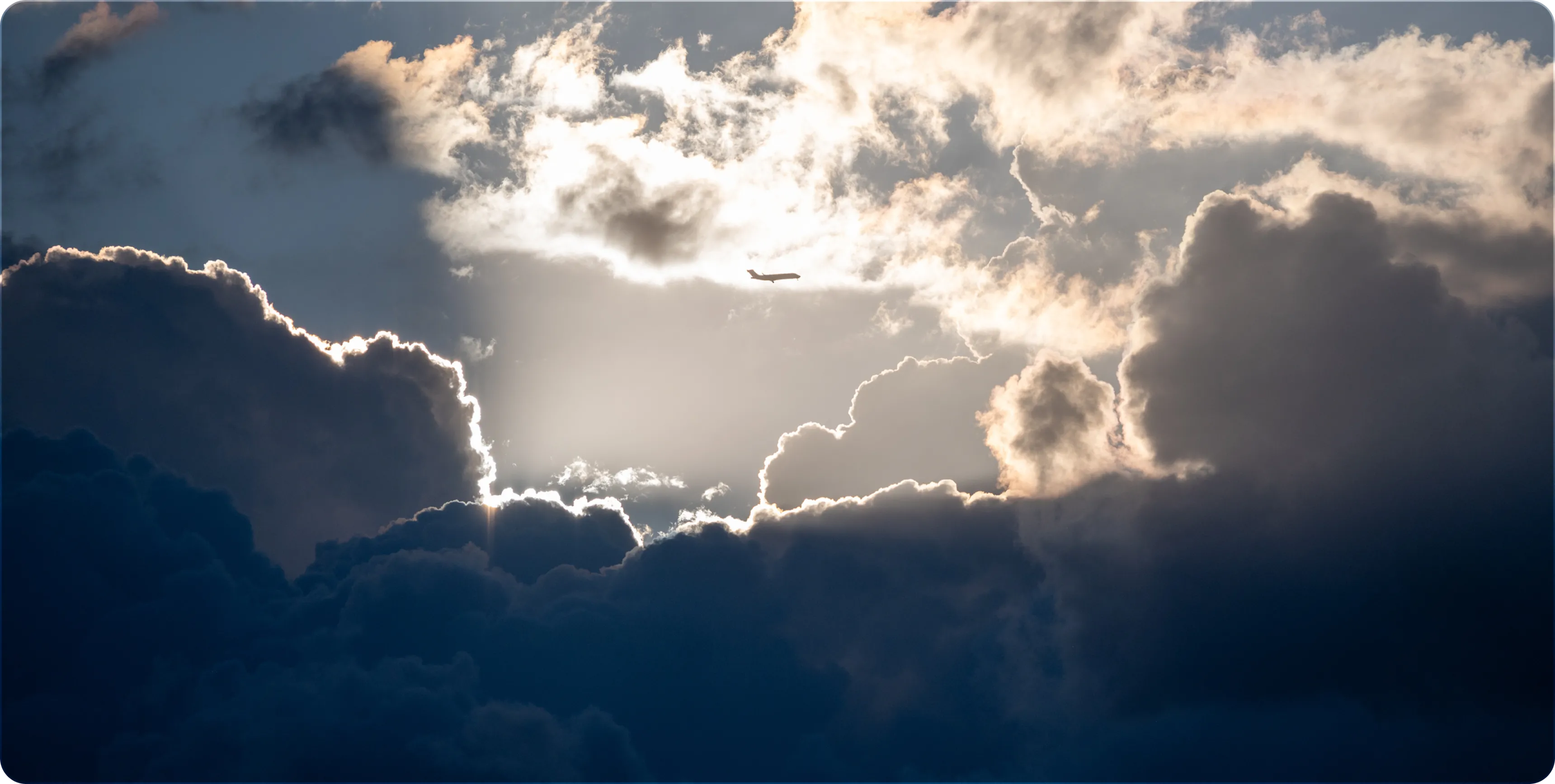 Airplane flying in the sky surrounded by dramatic dark and bright clouds with sunlight edges.