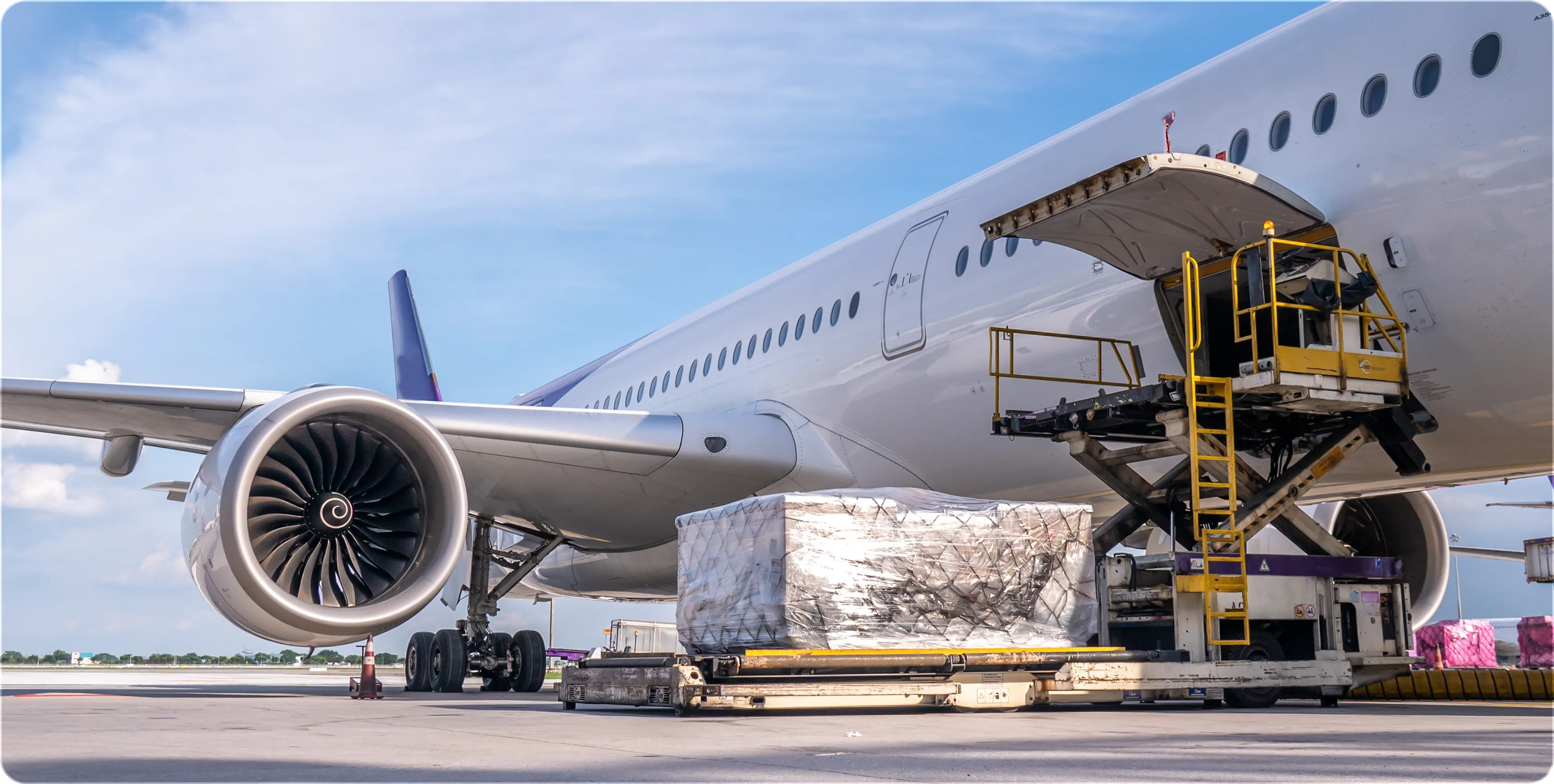 Cargo being loaded into an airplane through a raised platform at an airport under blue sky.