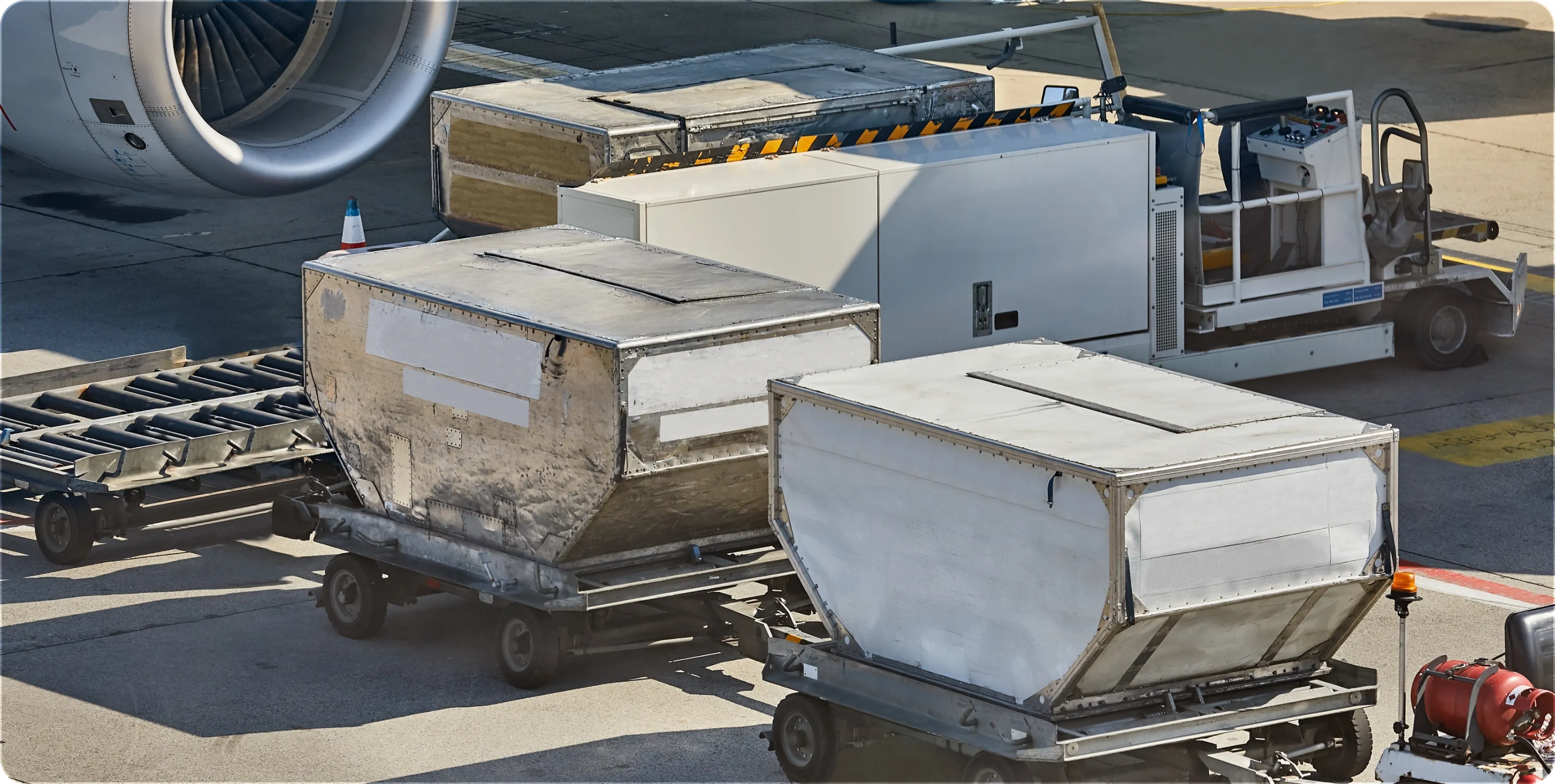 Baggage carts loaded and parked next to an airplane engine on airport tarmac.
