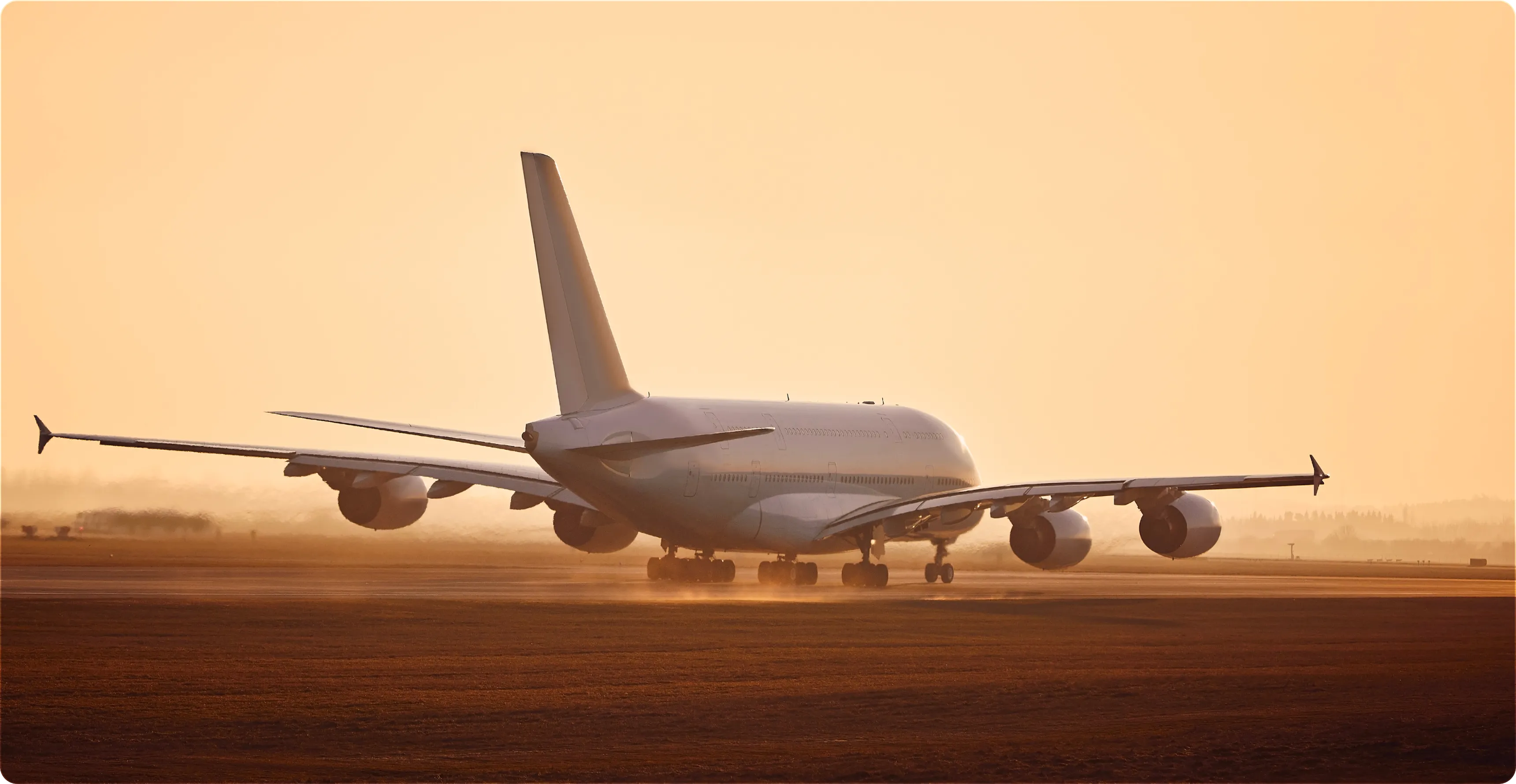 Rear view of a large airplane taxiing on a runway at sunset with a golden sky.