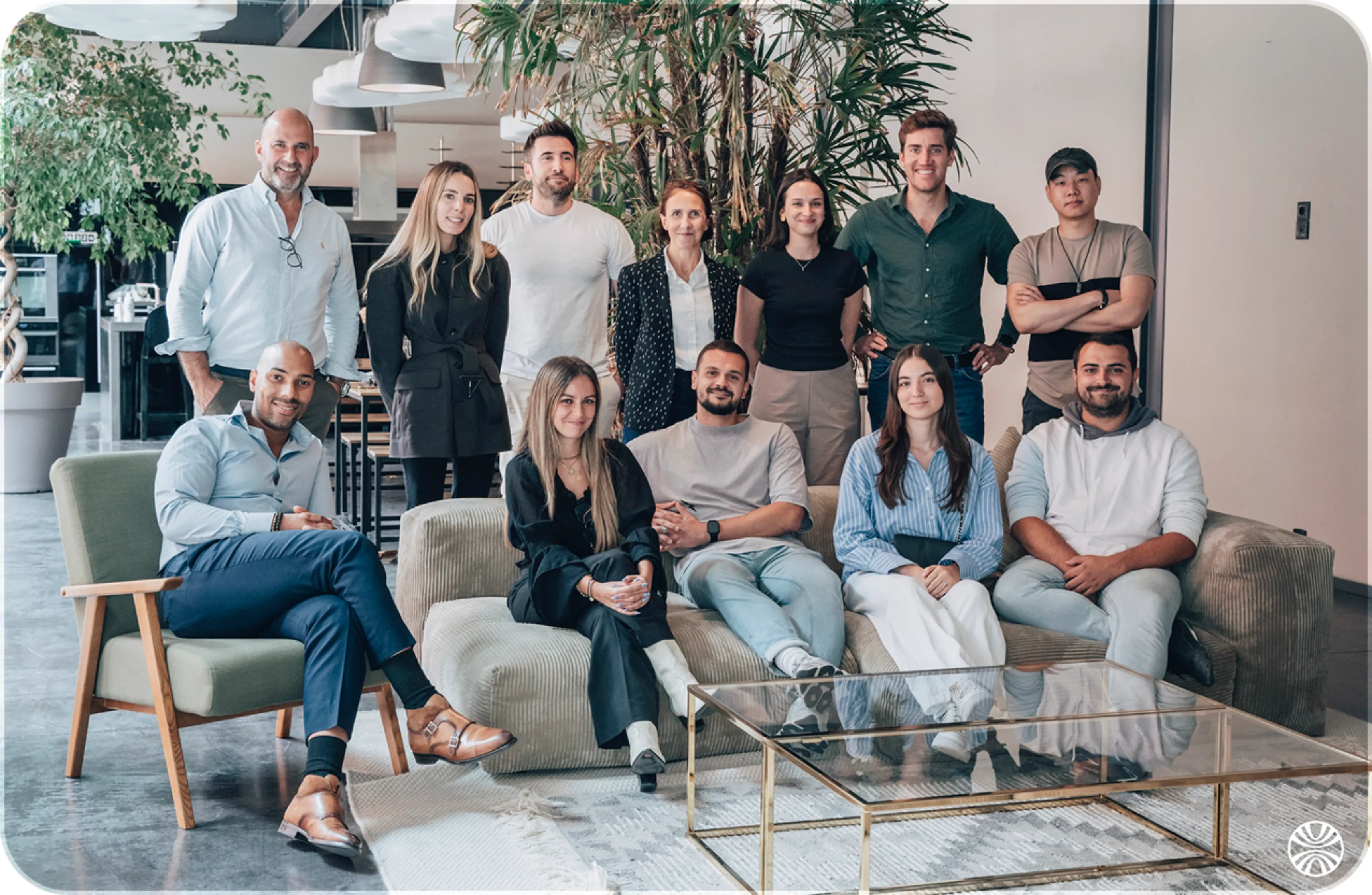 Group of diverse coworkers posing and smiling in a modern office lounge with plants and glass table.