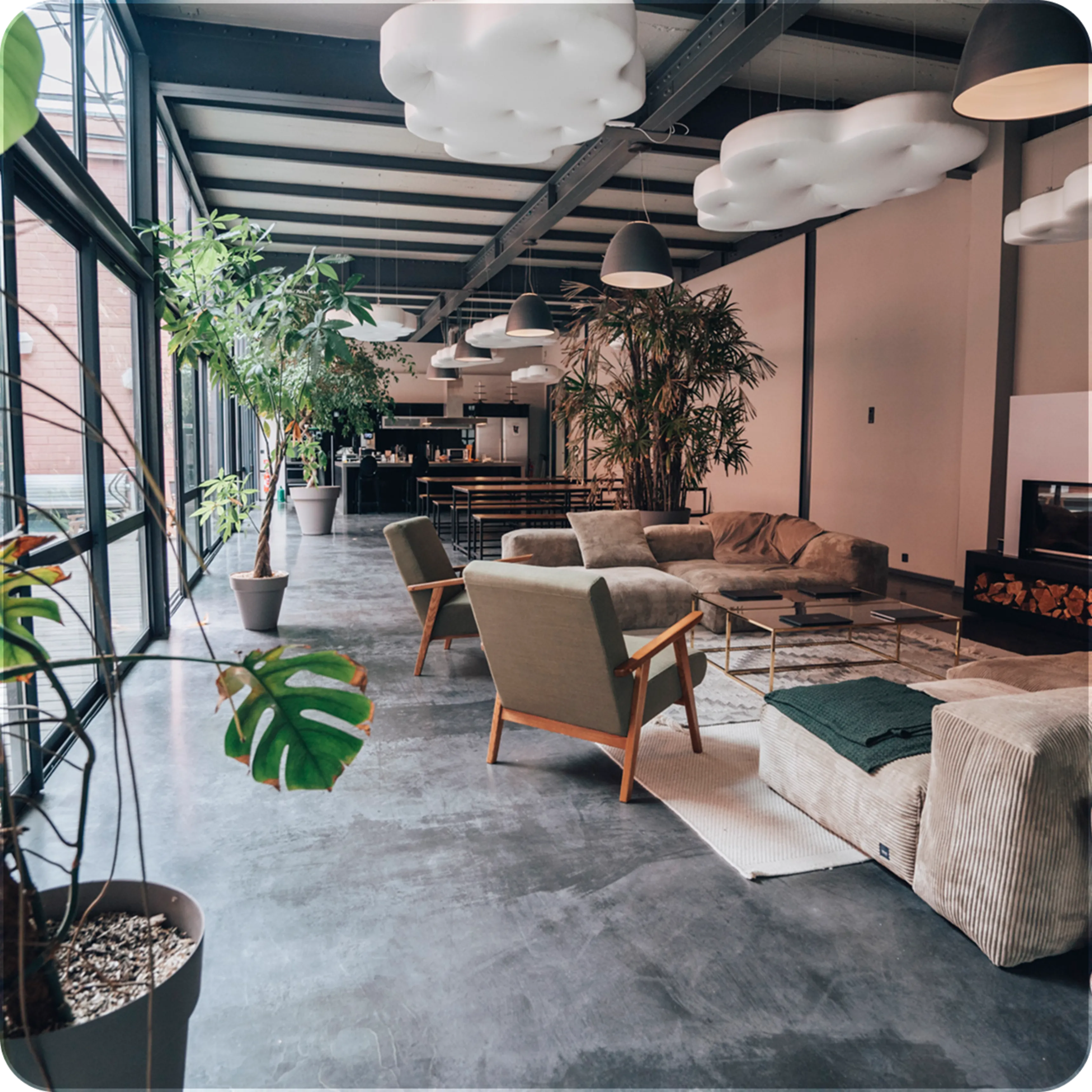 Modern open living space with large windows, plants, cushioned chairs, sofas, and cloud-shaped ceiling lights.