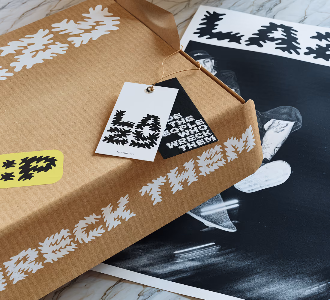 A LazyType Mockup showing a brown cardboard box with white text screen printed on it and a tag next to a black and white poster on a marble surface.