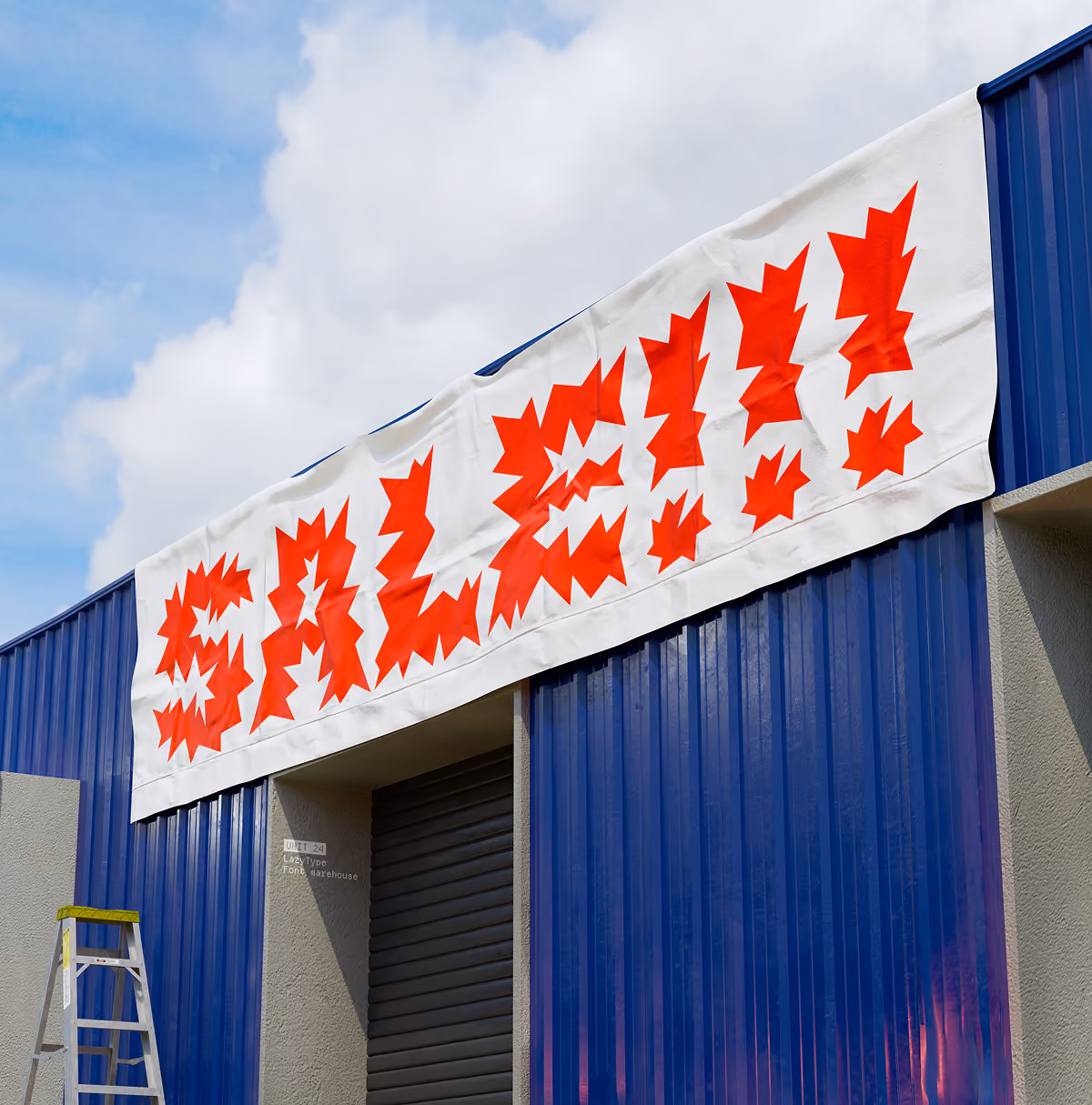 A LazyType Mockup with a large tarp sign that says SALE!!! hanging on blue warehouse building with ladder nearby.