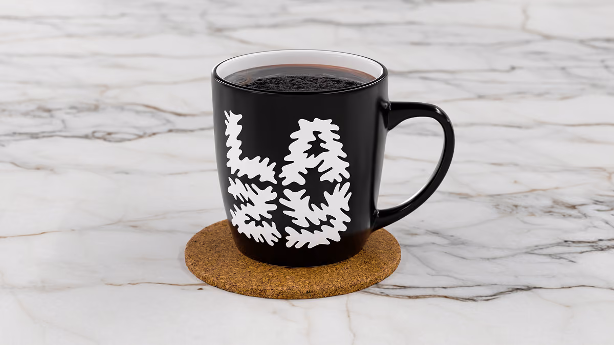 A LazyType coffee mug with white font on a cork coaster on a marble surface.