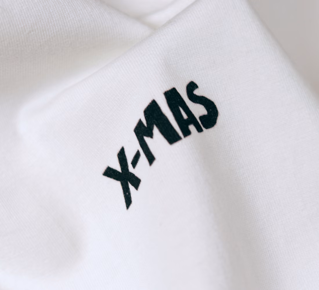 LazyType merch showing a close-up of white t-shirt fabric featuring small black "X-MAS" typography on the front chest.