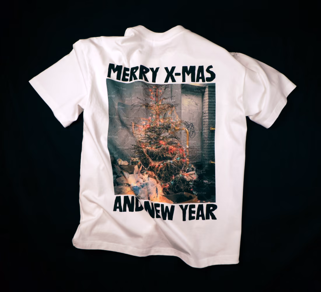 LazyType merch showing a white LazyType t-shirt laid flat displaying a back graphic of a trashed Christmas tree with text reading "MERRY X-MAS AND NEW YEAR"