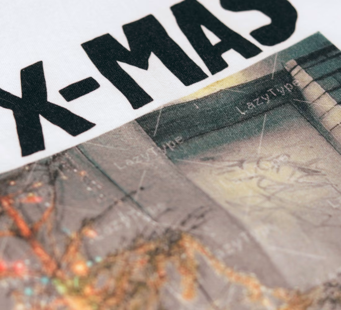 LazyType merch showing a macro close-up of white cotton fabric displaying bold black "X-MAS" screen-printed lettering over a photo graphic.