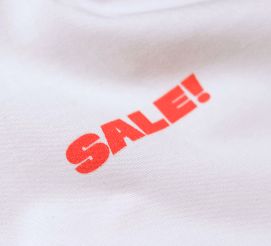 LazyType merch showing a close-up of white t-shirt showing a small red "SALE!" print on the front chest