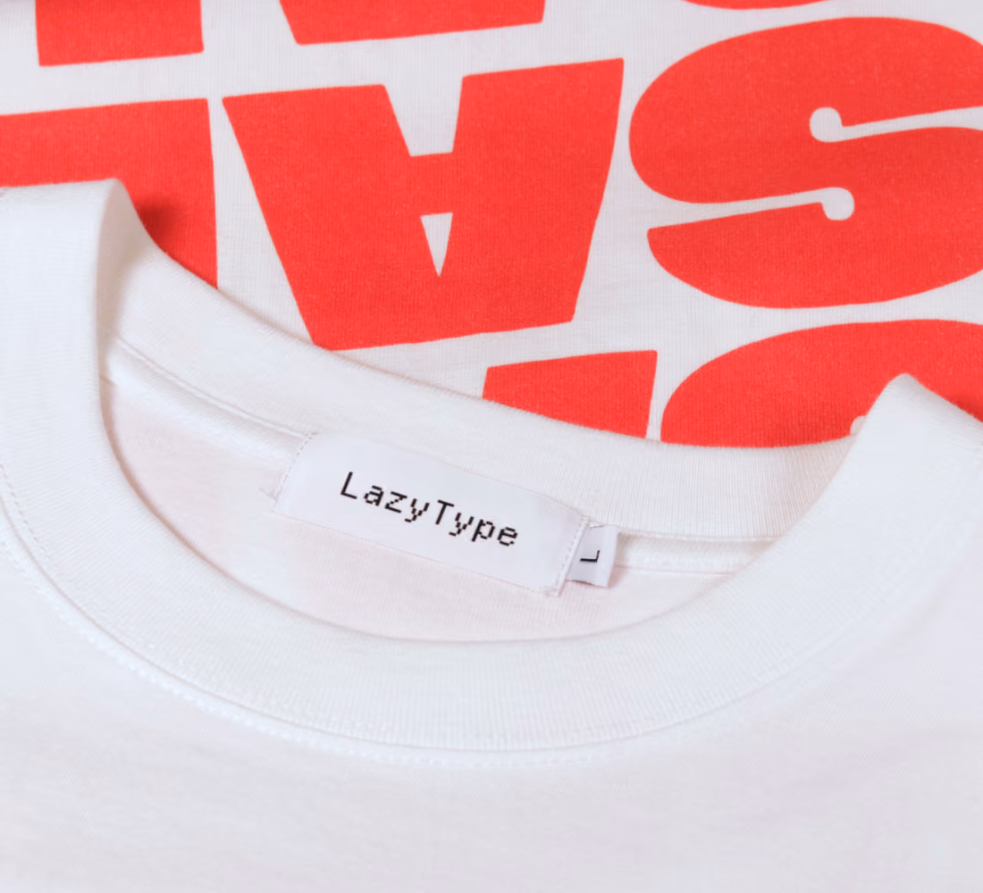 LazyType merch showing a close-up of a white t-shirt crew neck collar with a woven "LazyType" brand label and size "L" tag featuring bold red typography.