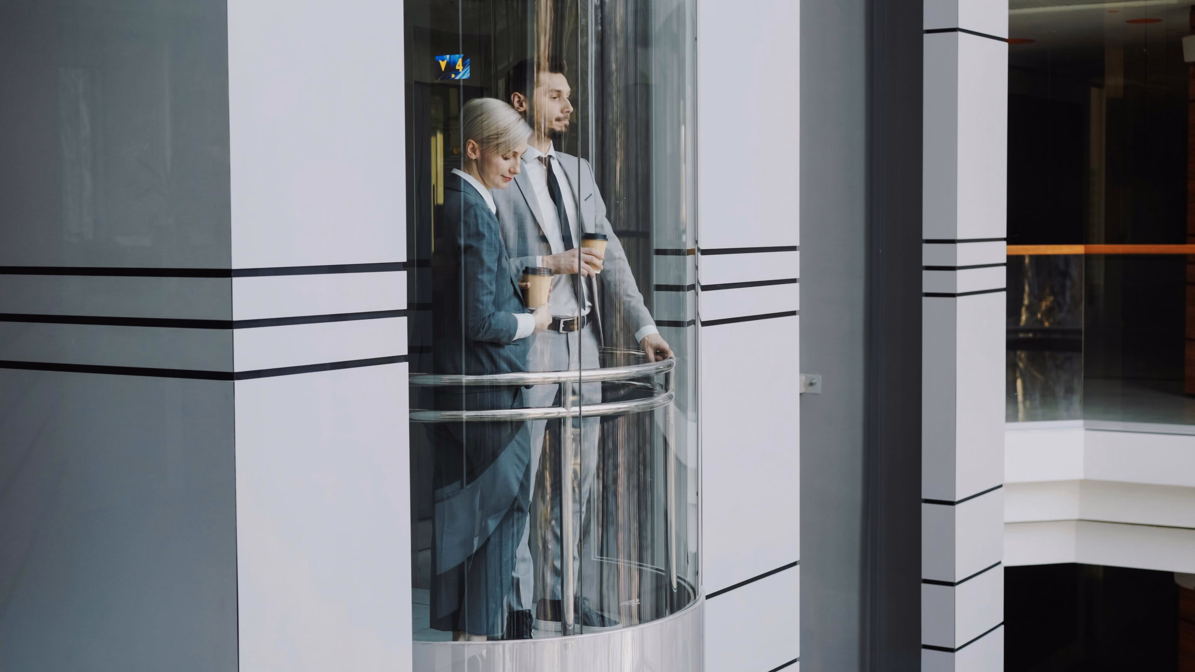 2 office workers waiting in a elevator with coffees in hand