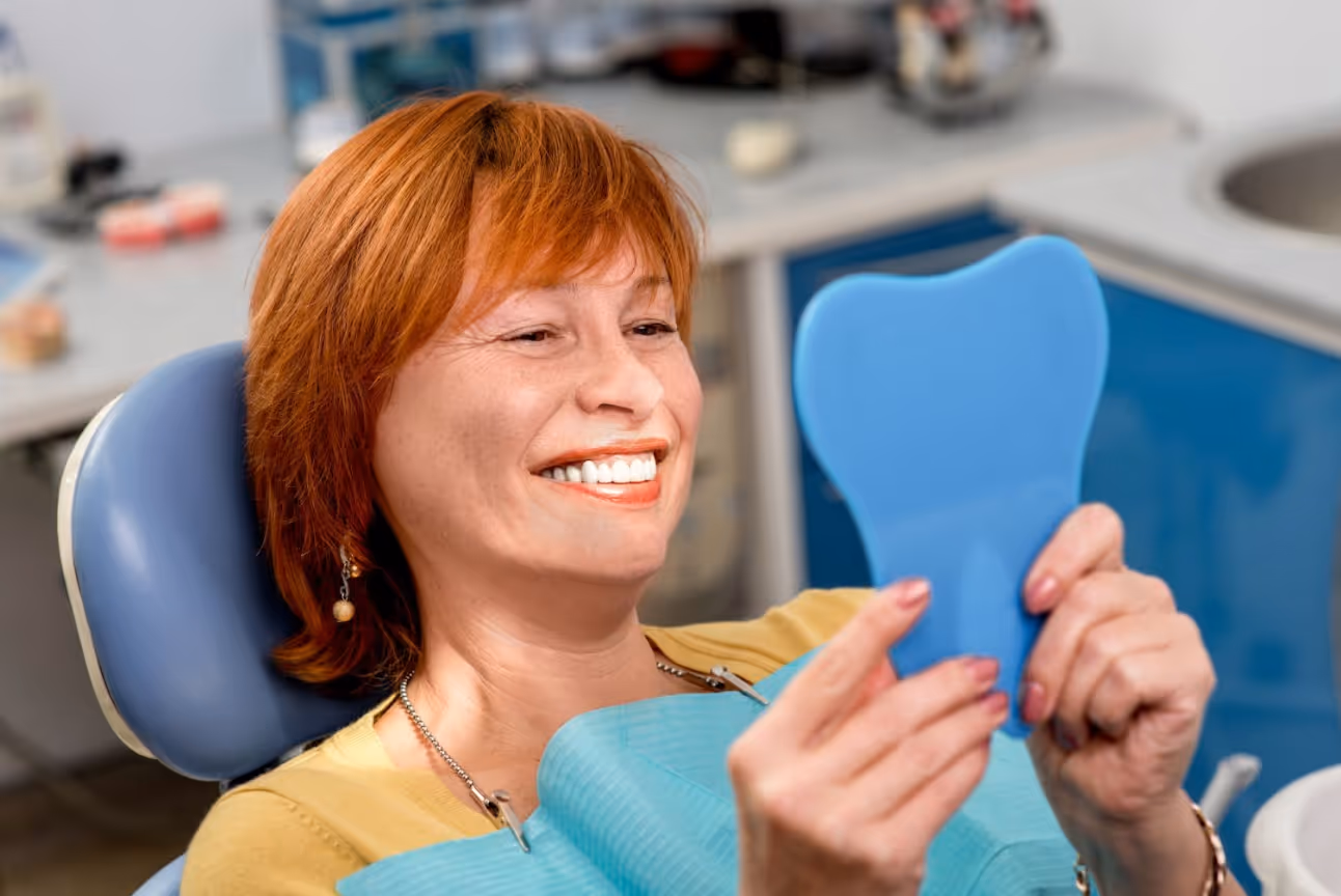 Woman smiling and checking her teeth in a hand mirror after a dental procedure