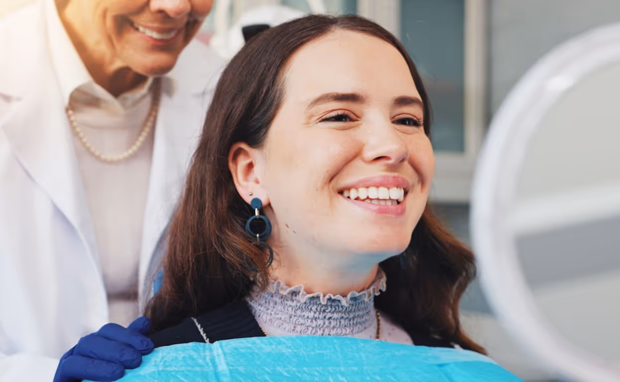 Woman smiling in a dental chair while viewing her teeth in a mirror after treatment.